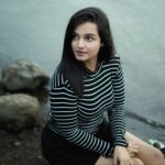 A young woman in a striped shirt sits by the riverbank in Bhopal, India, gazing thoughtfully.